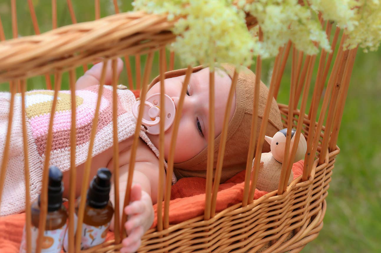 Baby liegt in Krippe und greift nach Babyduft SWEET DREAMS Körperöl.